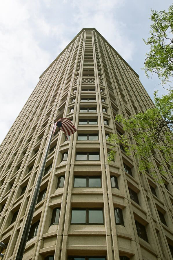 Looking up at the corner of a tall building. In front flies an American flag