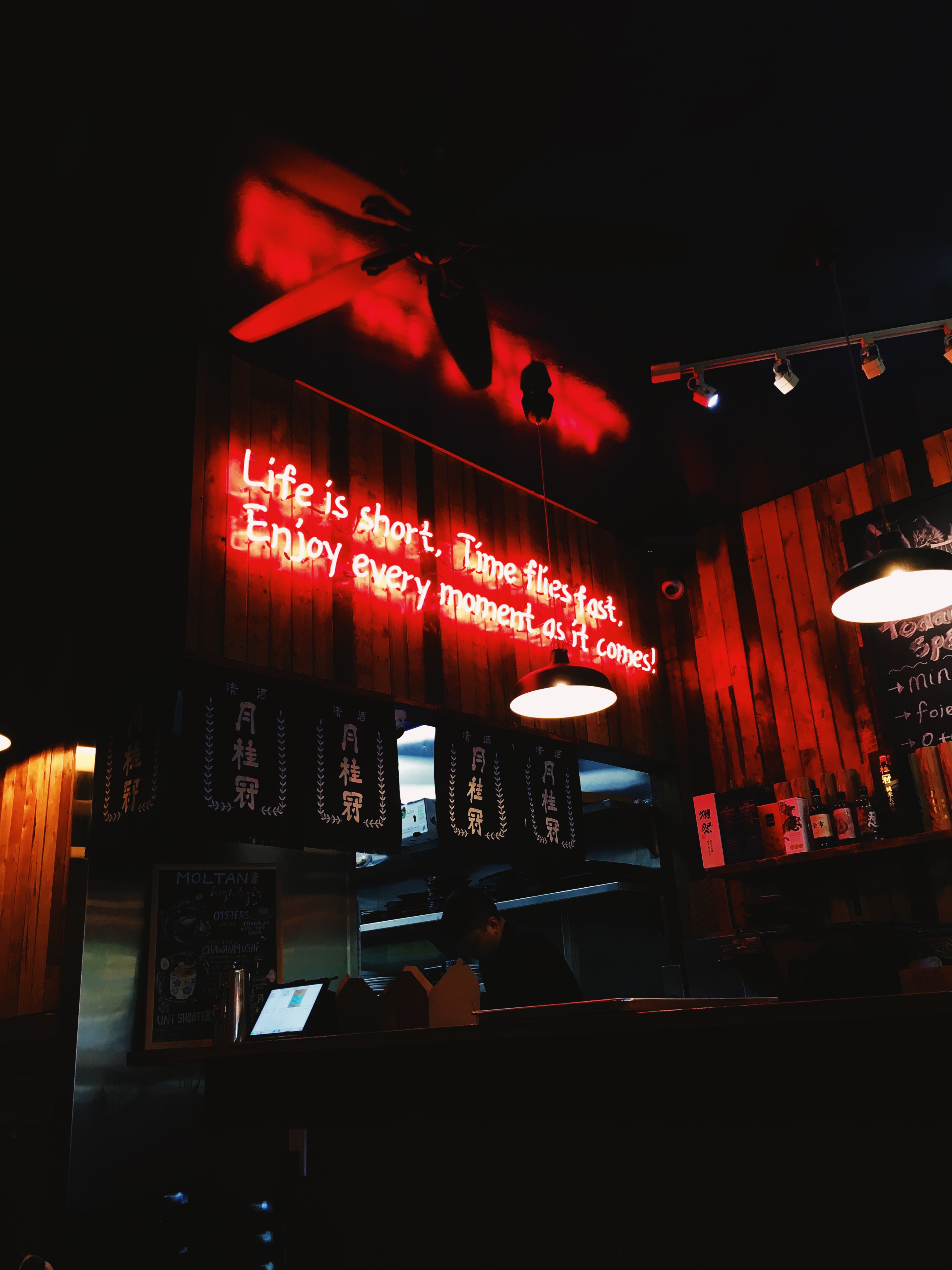A neon sign in a restaurant that reads 'Life is short. Time flies fast. Enjoy every moment as it comes!'
