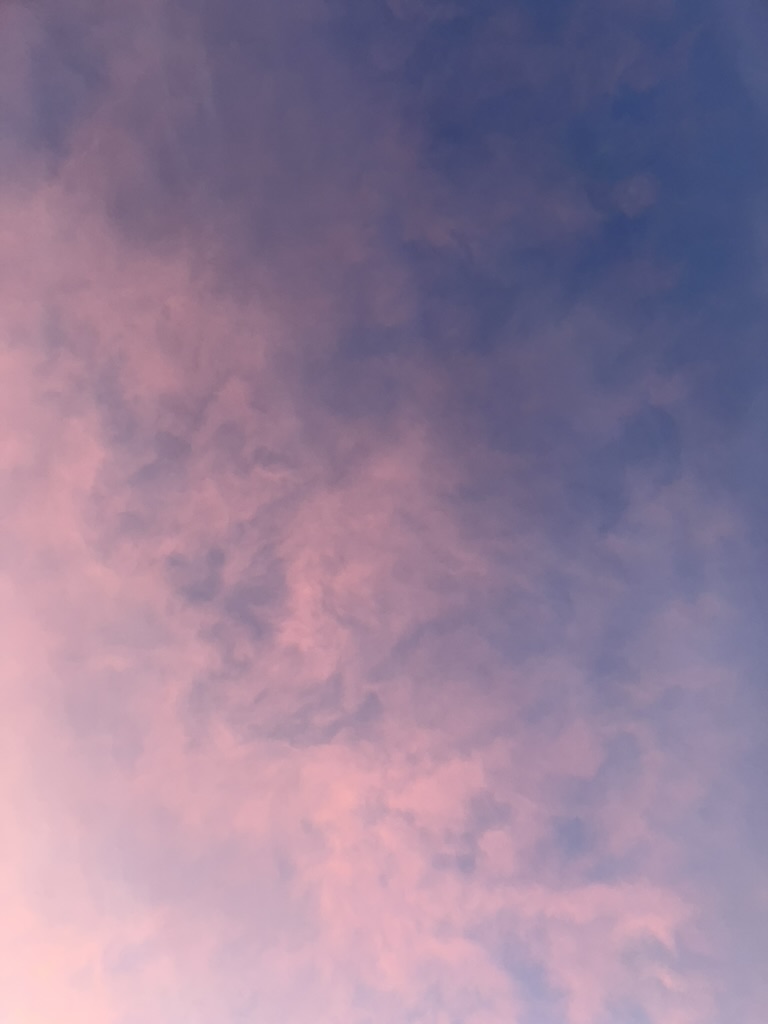 A pale blue sky at dusk with pink clouds.