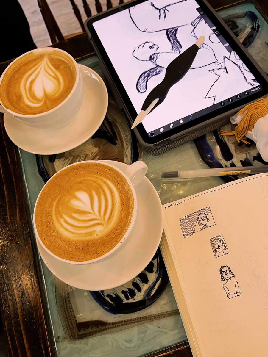 Cafe table with two lattes, and sketches on an iPad and notebook. 