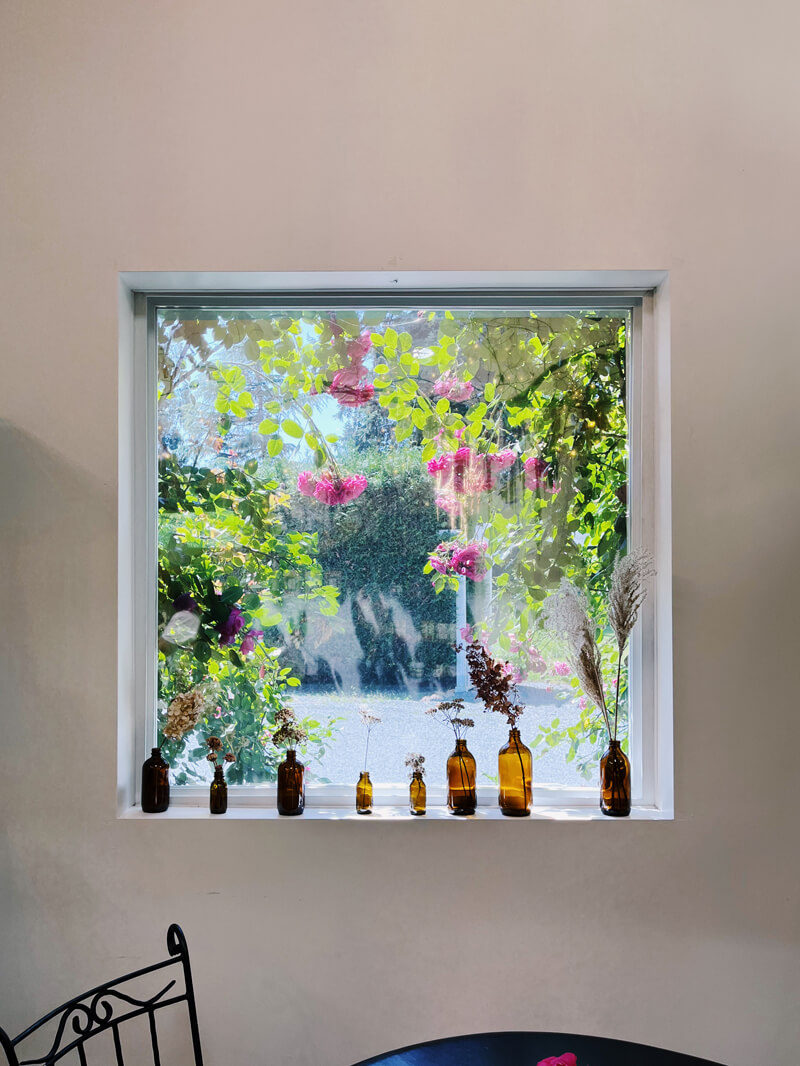 A square window looking out at trees. On the window sill are dried flowers in small bottles.