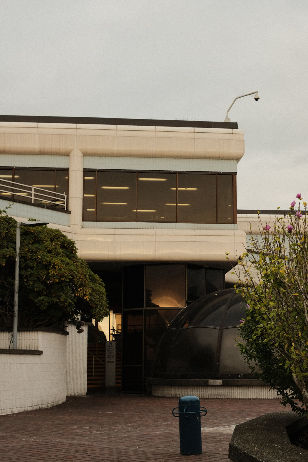 A path leading to a small building, which features large windows and rounded edges. The photo has warm tones and overcast.