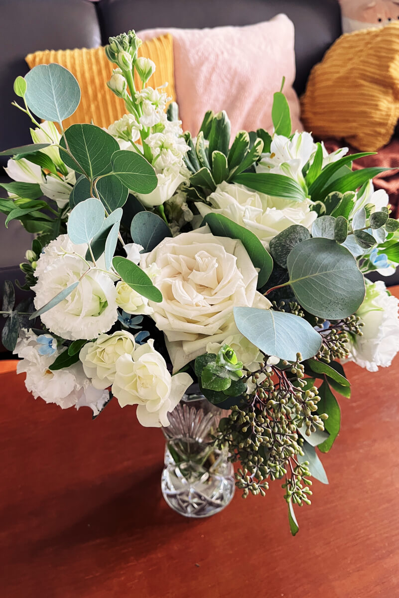 A pretty arrangement of white, soft yellow, and blue flowers in a vase. 