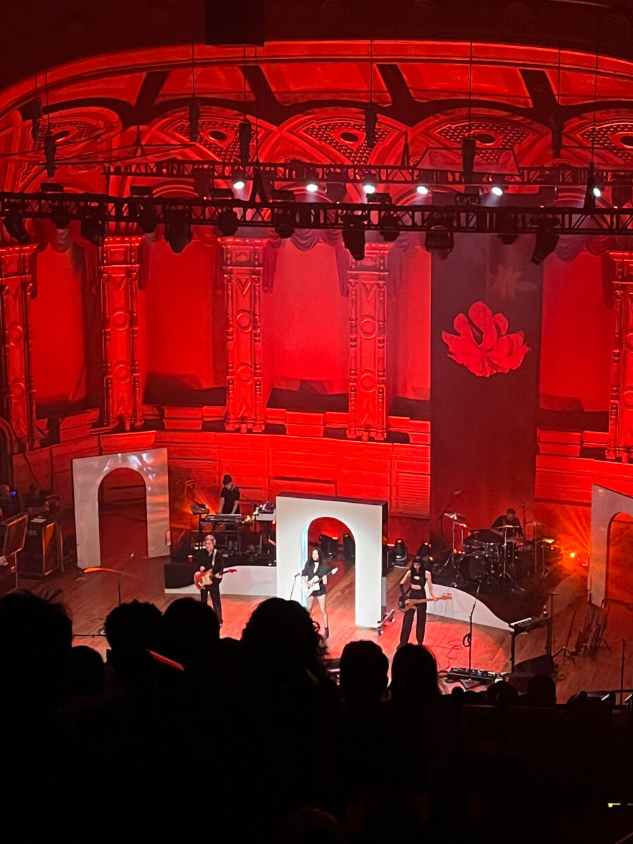 A low-quality photo of St. Vincent performing with her band on stage under red lights.