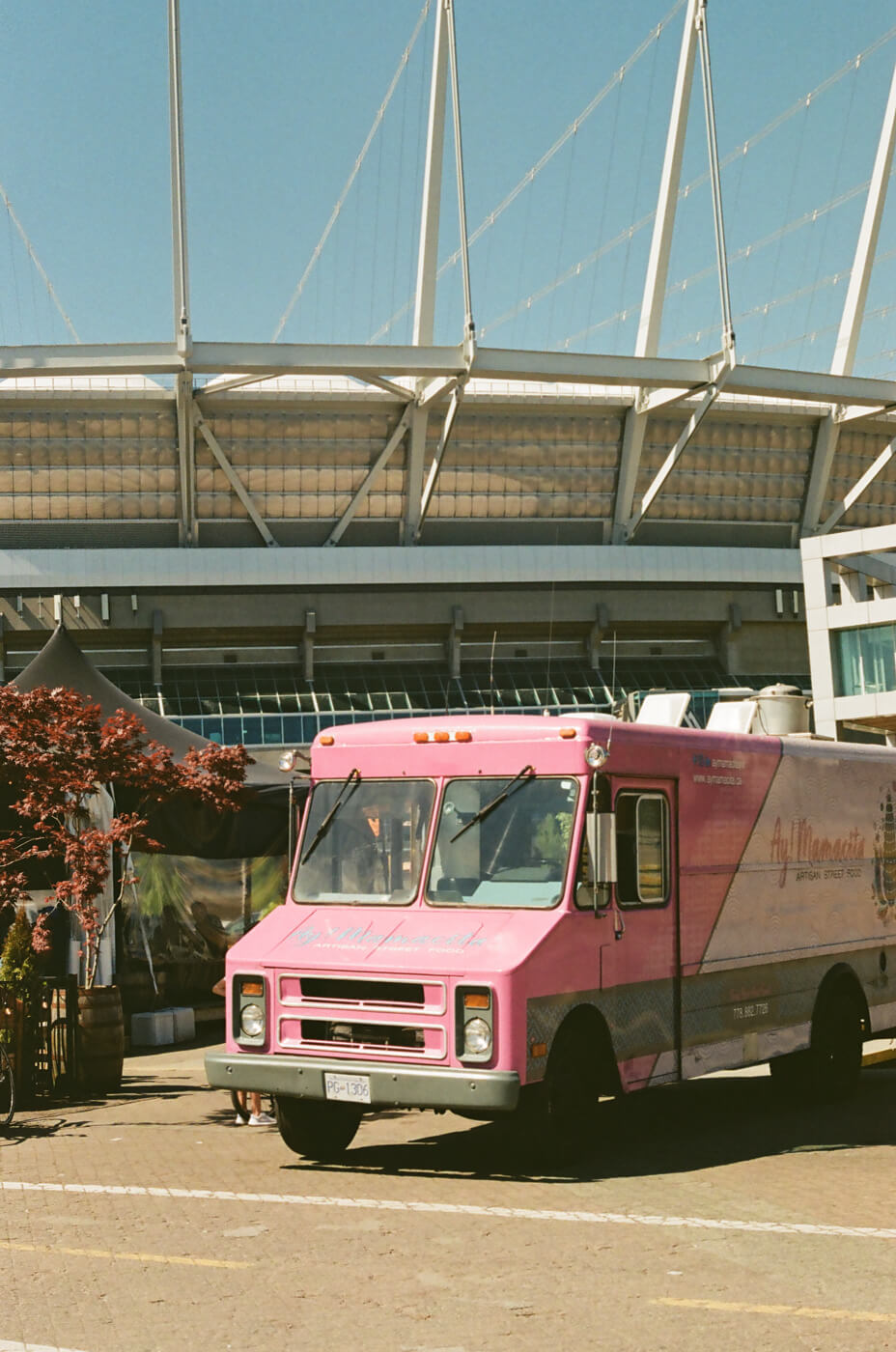 The closed side of pink and white food truck, which is parked in front of a sports stadium.