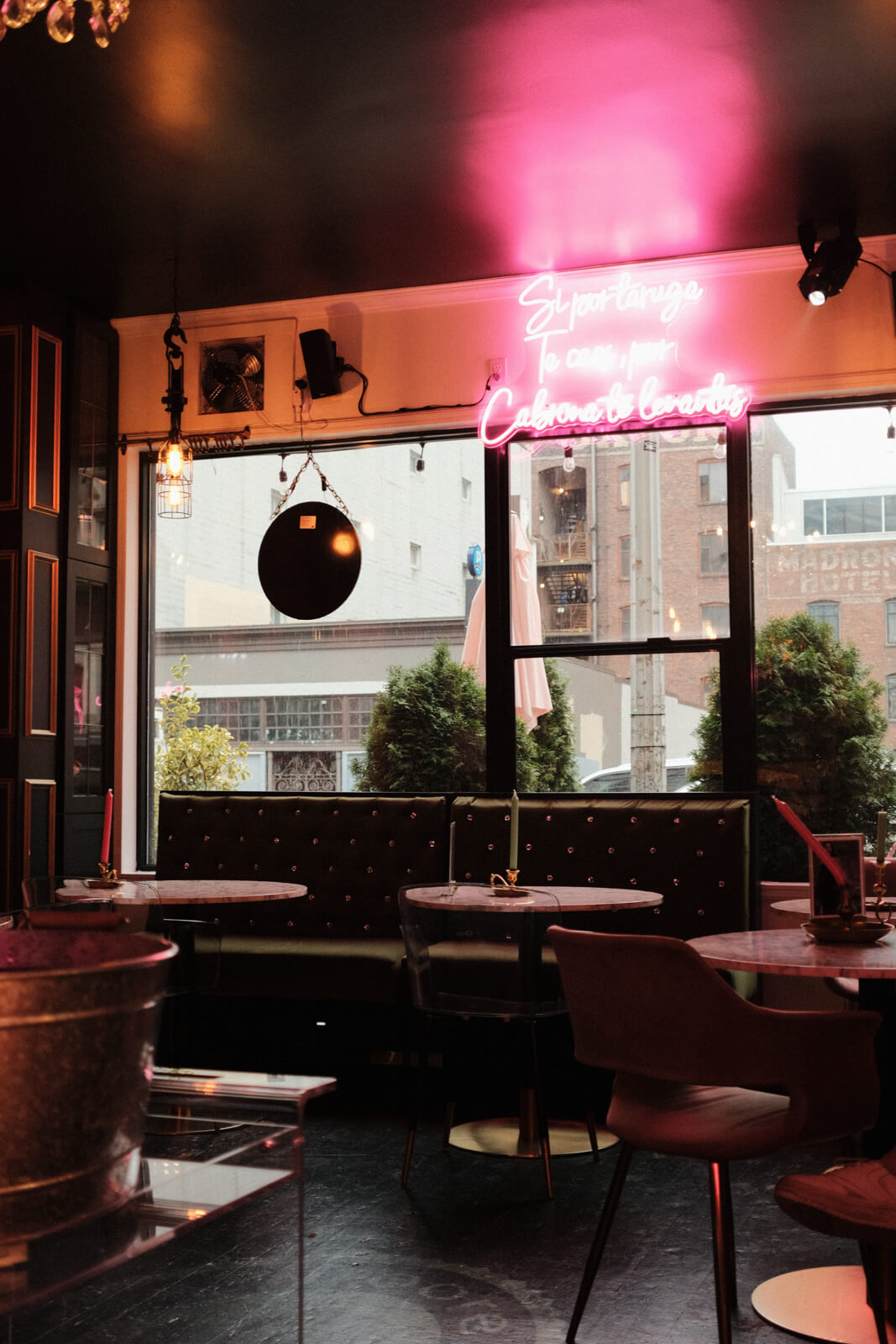 Coffee shop interior, which features plush seats, pink and green tones, and a bright pink neon sign written in Spanish.