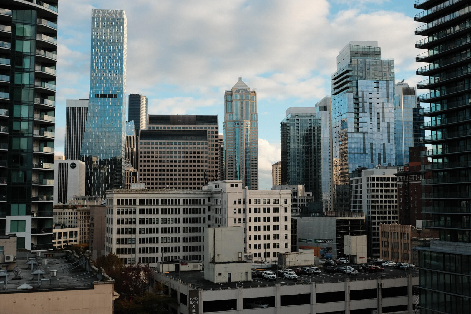 Seattle cityscape viewed from a high-up vantage point. A variety of building styles populate the skyline. One of the closer buildings has a parking lot on the roof.