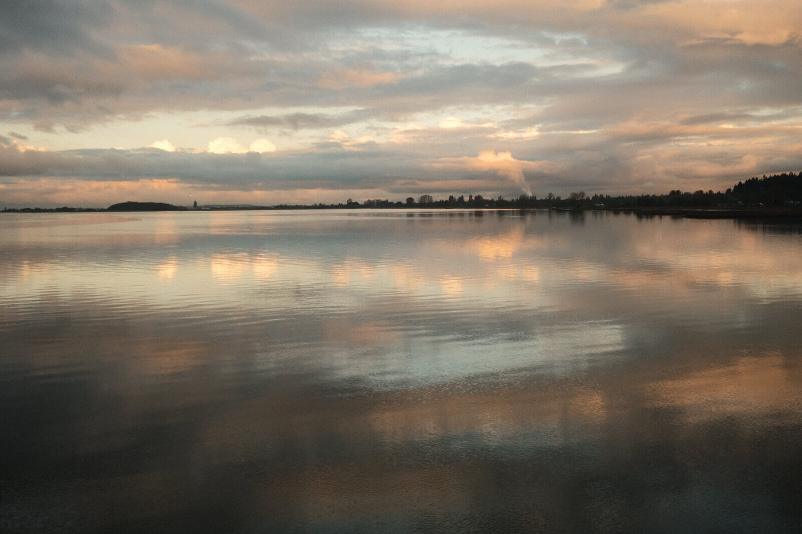 A view of the water, which has a mirror-like surface and reflects the dramatic clouds. Viewed in the morning, so some clouds reflect golden light.