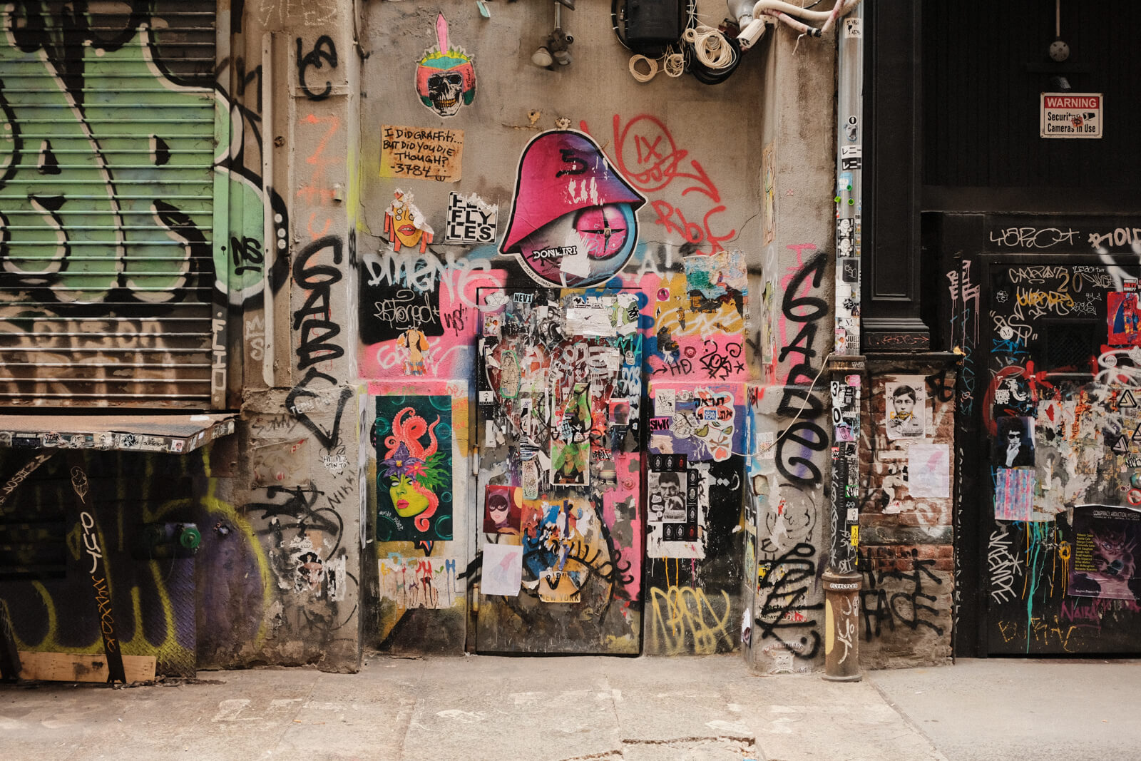 A wall in an alleyway covered with colourful graffiti, ripped up posters, stickers, and other such street artwork.