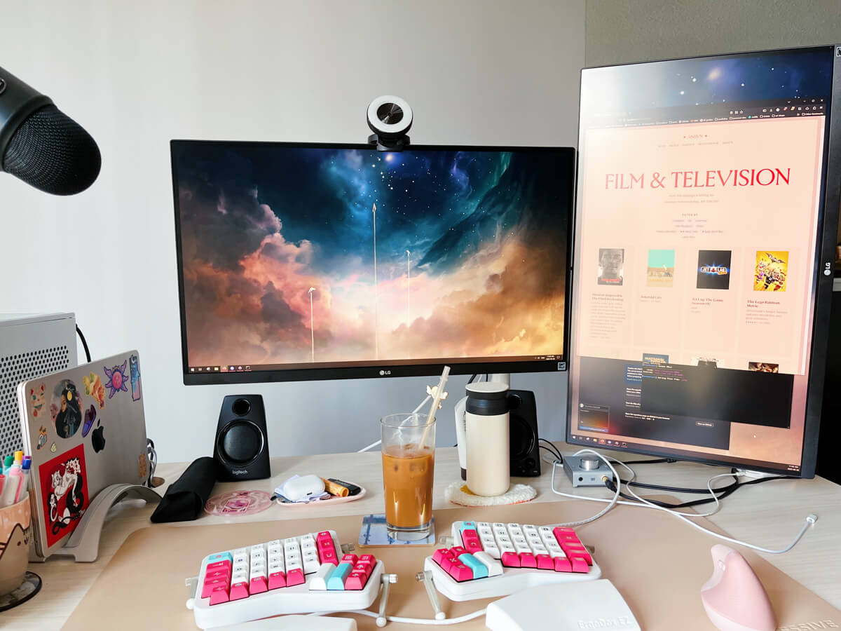 My desk, with my website open in one of my two monitors, showing my work in progress site redesign. I have a glass of iced coffee.