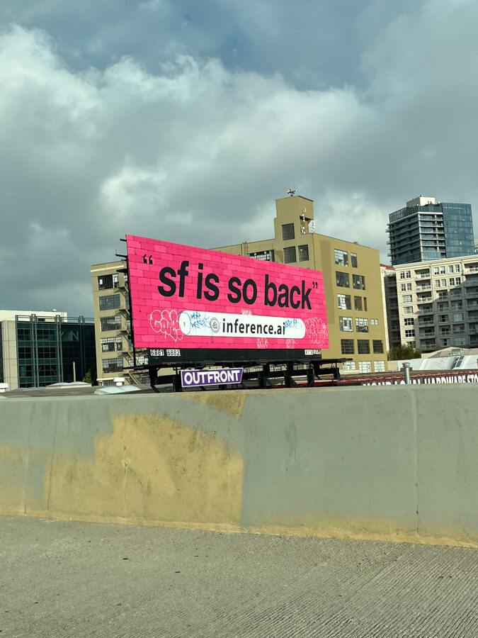 A billboard on the side of the highway that says “SF is so back”, in quotation marks. It points to the website inference.ai.