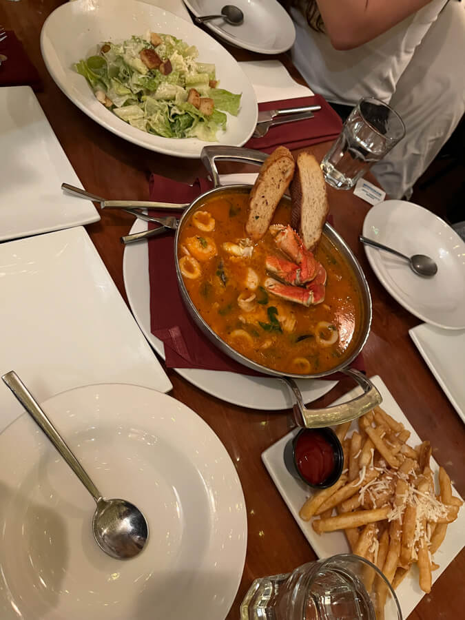 Table with seafood stew, salad, and fries.