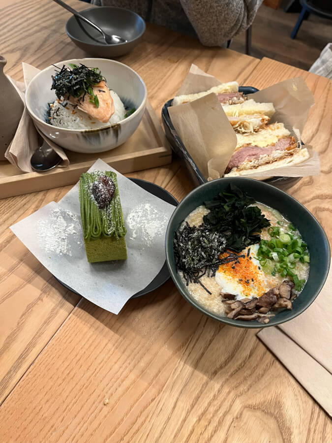 A bowl of chicken porridge, salmon on rice, some katsu sandwiches, and a macha roll cake.
