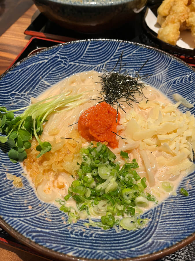A bowl of mentaiko udon, which is topped with seaweed strips, some greens, and a ball of mentaiko.
