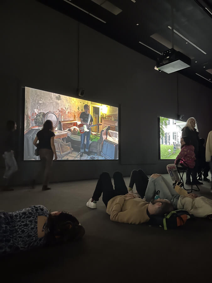 Inside the exhibit, where people are lying on the floor listening to music. The musicians are projected on screens all around the room.