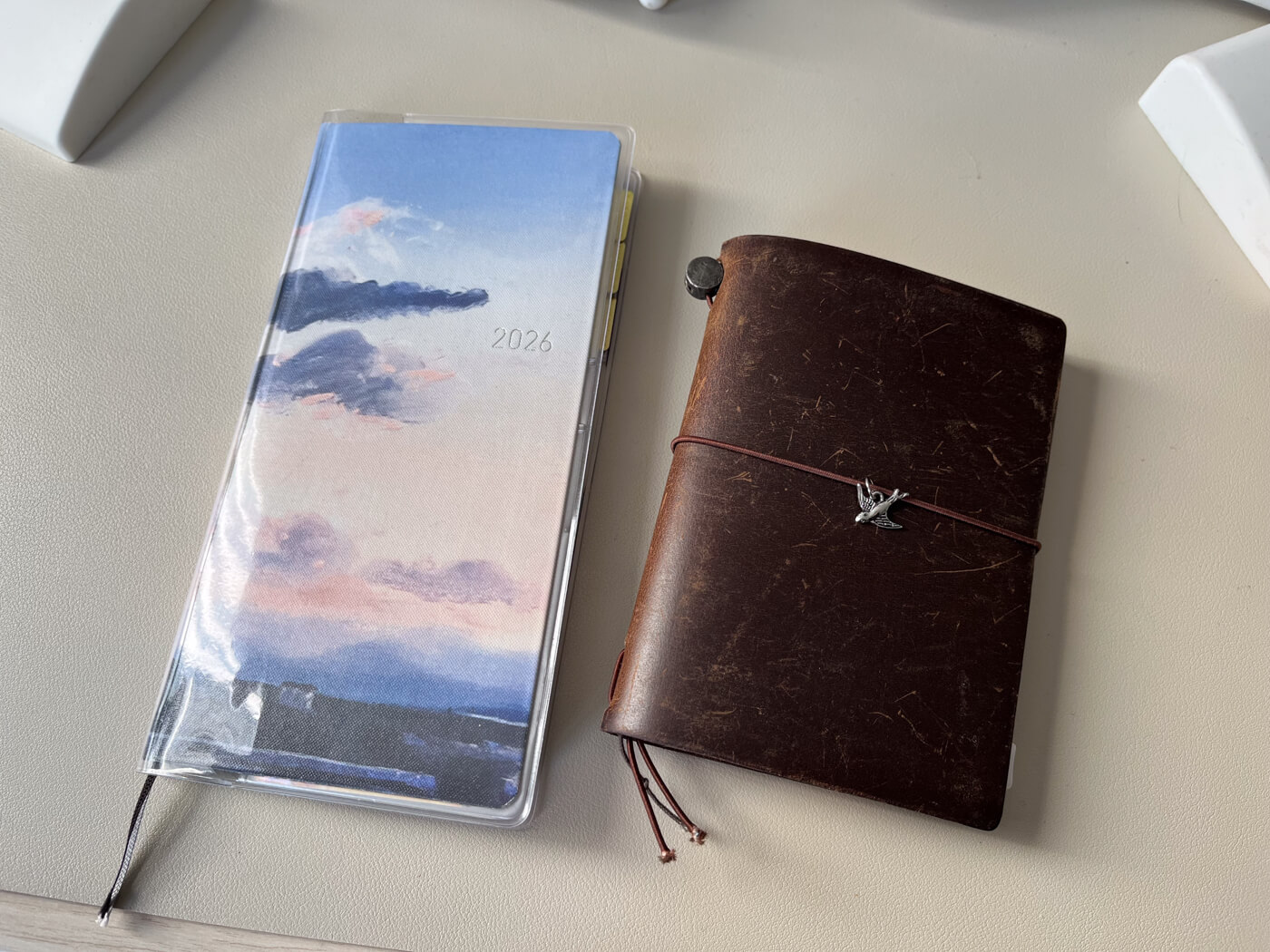 My Hobonichi Weeks planner, which features the cover with the purple pink sunset painting, and my brown Traveler’s Notebook.