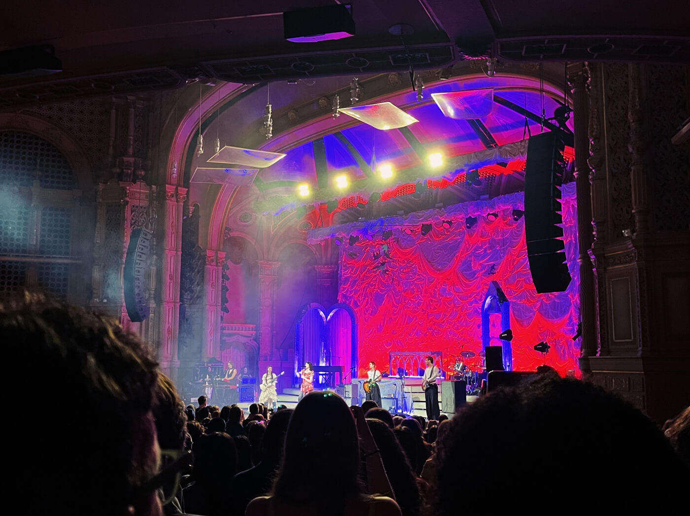 A distant, poor quality concert photo of a five-piece band on stage against a vivid red and purple backdrop. 