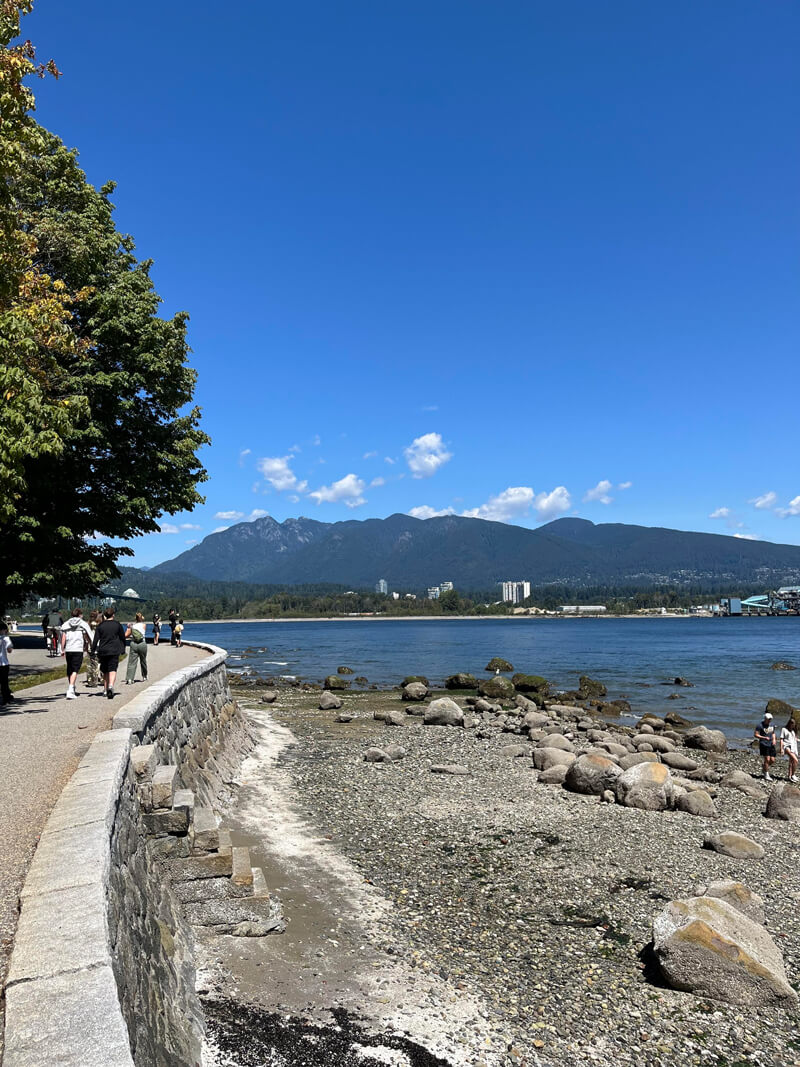 The Vancouver seawall, showing a winding pedestrian path next to ocean, forest, and mountains.